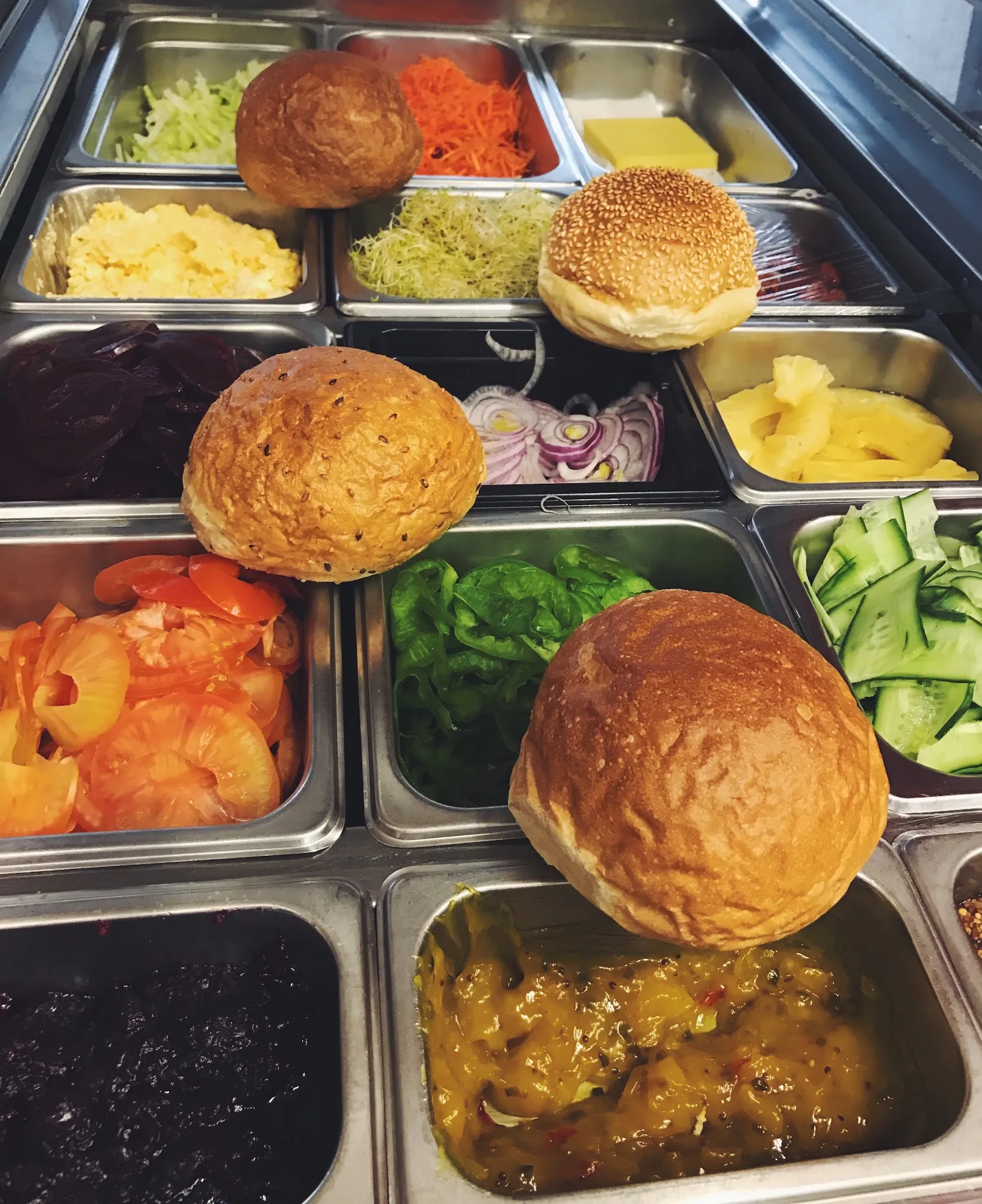 Sandwich prep station with bread rolls over fresh salad ingredient trays