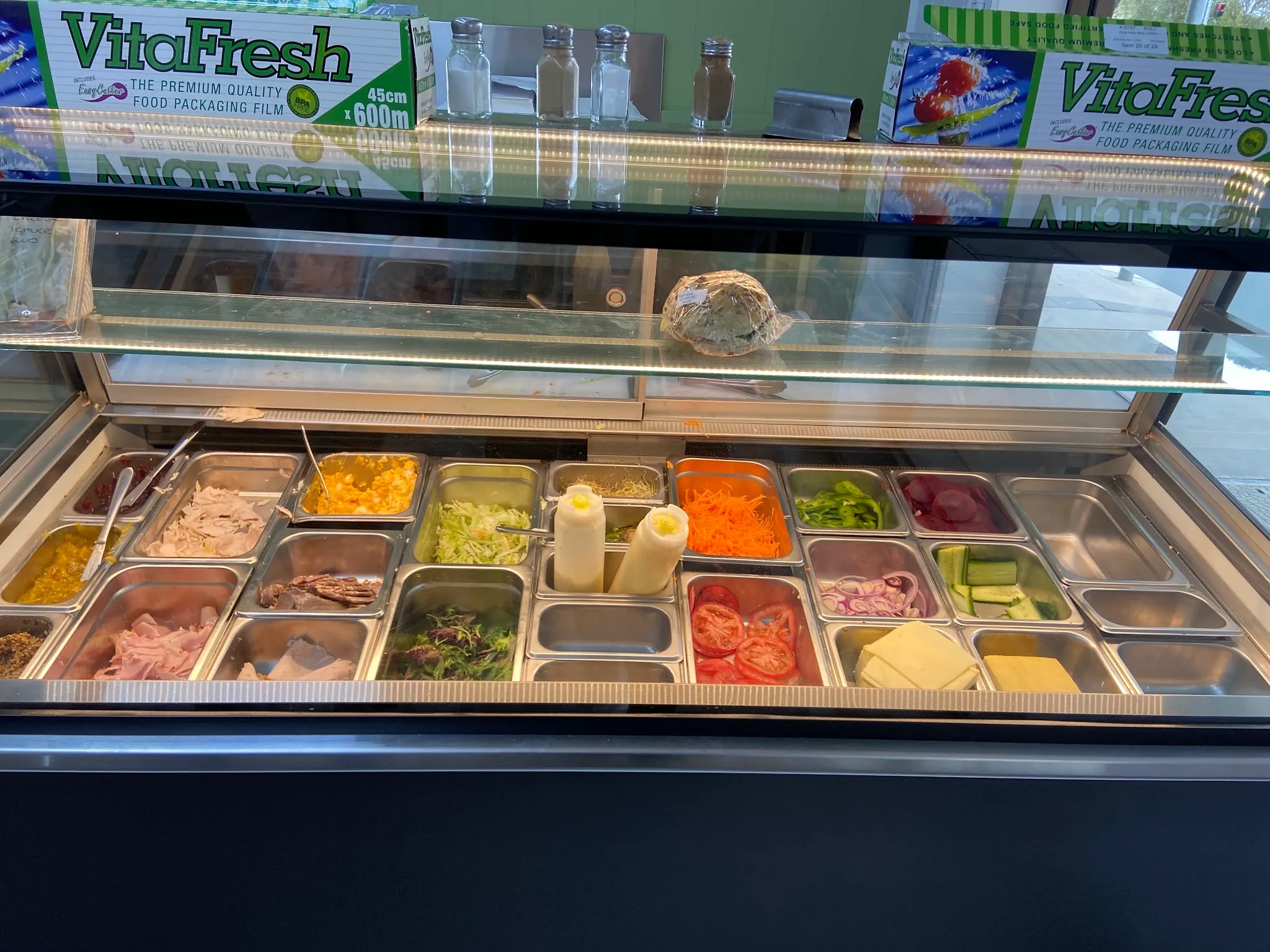 Sandwich bar fridge with meats, salad and condiments in metal trays