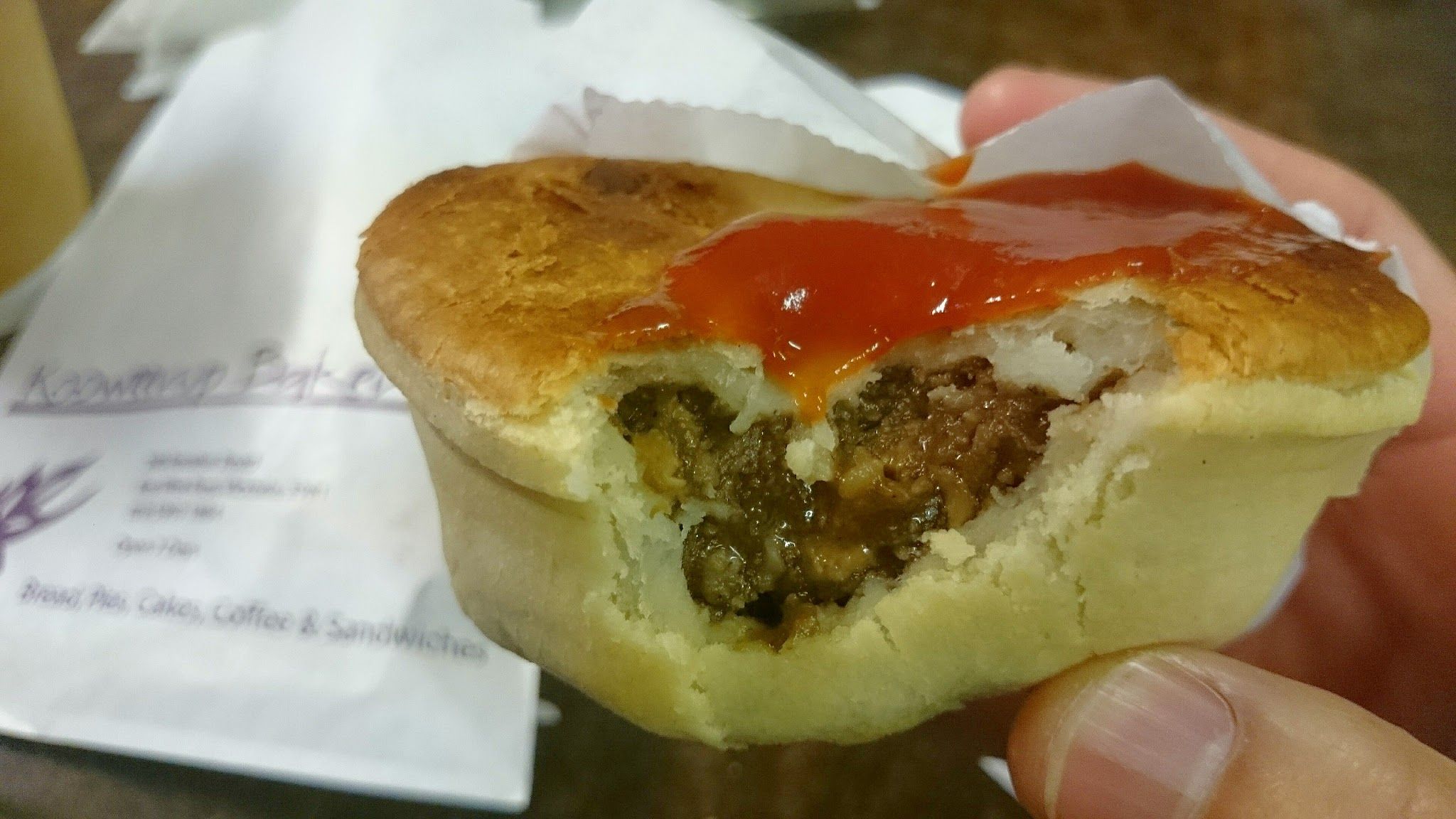 Bitten meat pie with tomato sauce, Kooweerup Bakery packaging visible behind